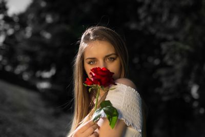 Close-up portrait of young woman holding red rose