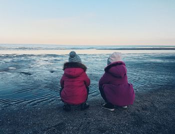 Rear view of women crouching on beach against sky