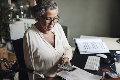 Businesswoman with disability scanning documents through smart phone while sitting at home office