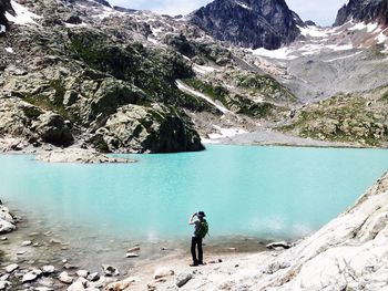 Man standing on rock by lake against sky