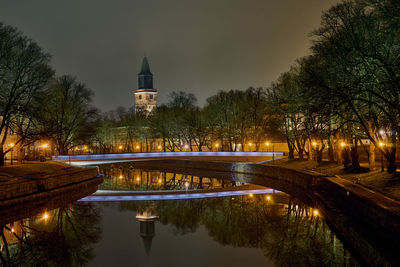 Illuminated building by lake against sky at night