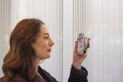 Woman holding camera while standing by window