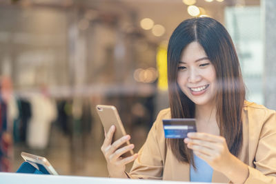 Close-up of smiling woman holding credit card while using mobile phone
