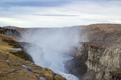 Scenic view of waterfall against cloudy sky