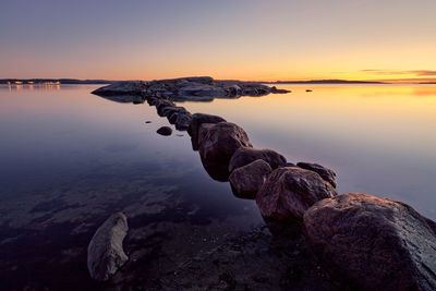 Rocks at sea shore against sky during sunset