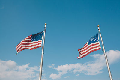Low angle view of american flags fluttering against blue sky