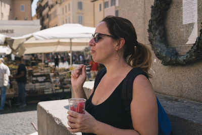 Midsection of woman drinking glass while sitting in city