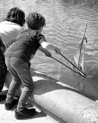 Rear view of siblings playing with toy boat in lake