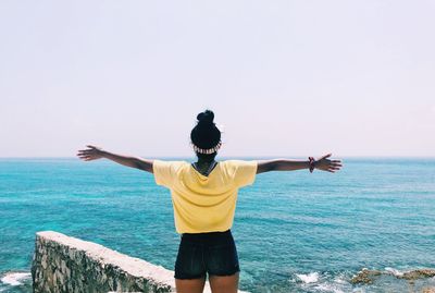 Rear view of woman with arms outstretched looking at sea against sky