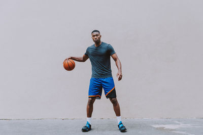 Full length portrait of young man playing basketball against wall