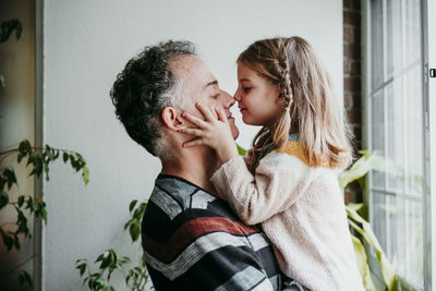 Daughter rubbing nose with father while standing by window at home