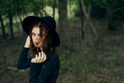 Portrait of young woman wearing hat standing in forest