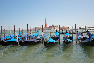 Gondolas moored in canal against clear sky