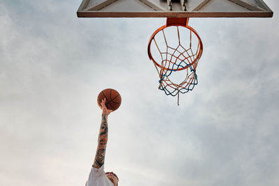 Hand of man throwing basketball to the basket hoop. basketball hoop and ball against cloudy sky