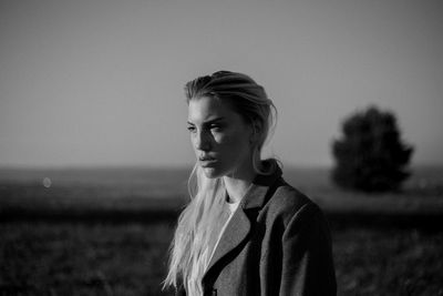 Portrait of young woman looking away on field against sky