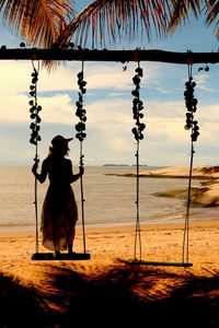 Silhouette woman sitting on swing at beach