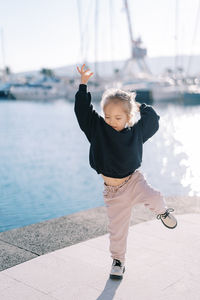 Side view of boy playing with arms raised standing against sea