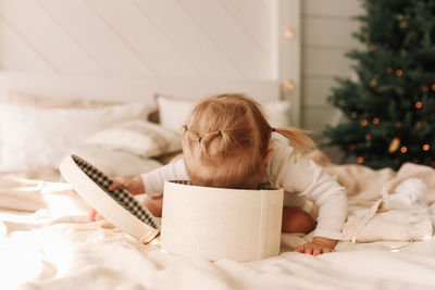 Funny funny little girl baby opens christmas gift box sitting on bed at home on holiday