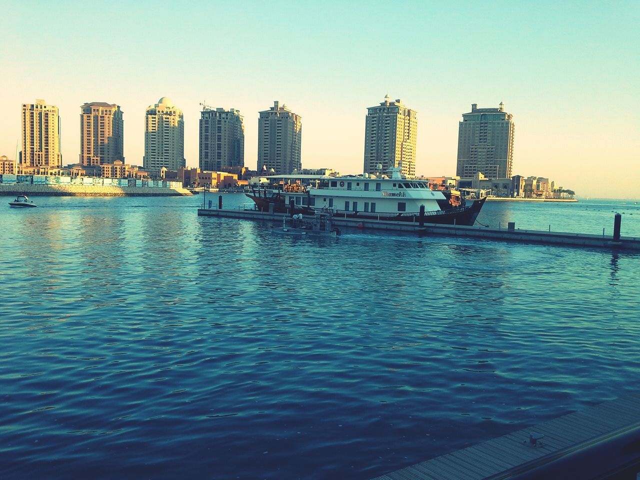 water, building exterior, architecture, built structure, sea, city, clear sky, waterfront, nautical vessel, incidental people, sky, blue, transportation, rippled, boat, cityscape, outdoors, building, residential building, river