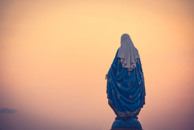 Rear view of woman standing against orange sky