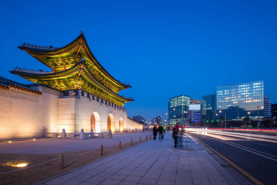 People walking on street against illuminated buildings at night