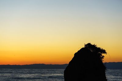 Silhouette of cliff at seashore during sunset