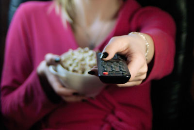 Midsection of woman having popcorn while changing tv channel