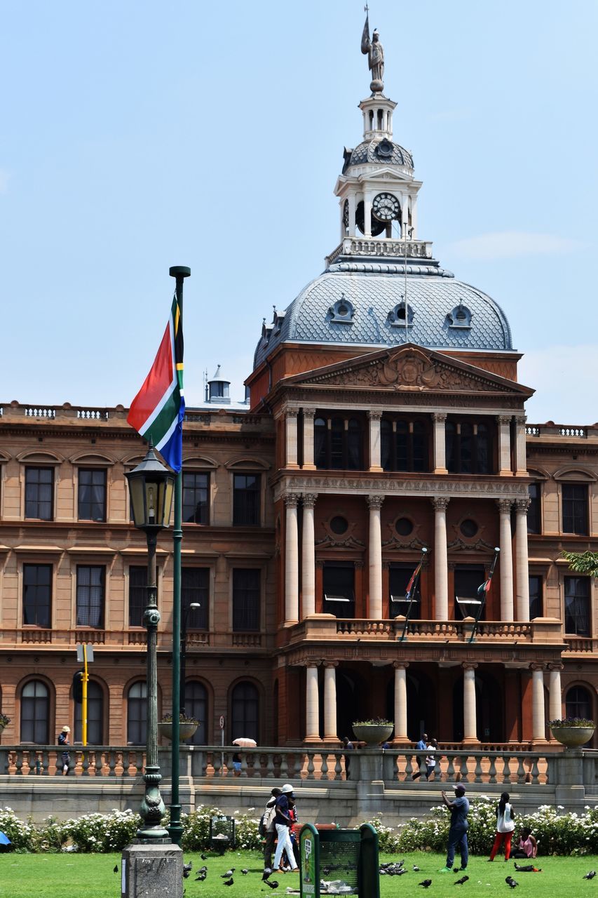 flag, architecture, building exterior, patriotism, built structure, day, large group of people, outdoors, real people, pride, clear sky, travel destinations, dome, men, grass, sky, city, politics and government, people