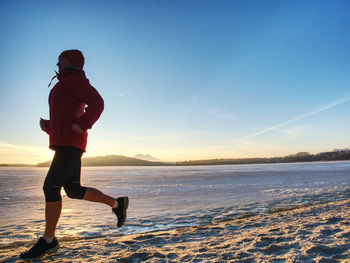 Young woman running along the shore of a frozen lake in winter spring. regular training run, keep 