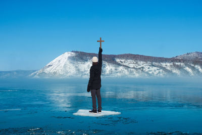 Rear view of man standing on mountain against blue sky