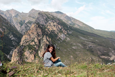 Side view of young woman sitting on field against mountain range