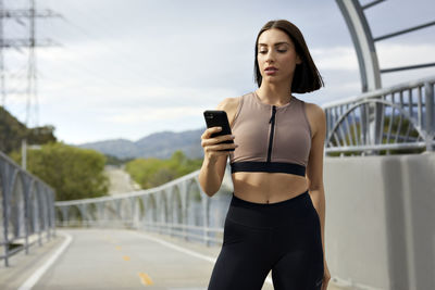 Jogger text messaging on smart phone while standing at bridge