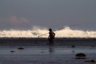 Man fishing at beach against sky