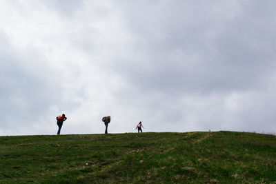 People walking on field against cloudy sky