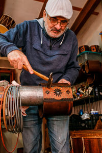 Professional male master using hammer while making shell of drum with creative patterns while working in light workshop with special instruments