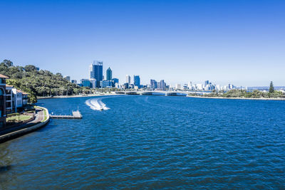 Scenic view of river and buildings against clear blue sky