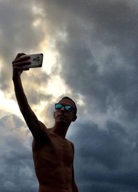 Low angle view of hand holding smart phone against sky