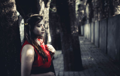 Young woman by tree standing on sidewalk