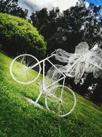 Bicycle parked by tree on field against sky