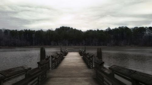 Empty wooden pier over lake against sky