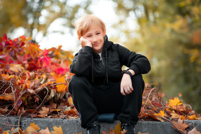 Boy sitting on maple leaves during autumn