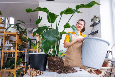 Portrait of young woman standing by potted plant