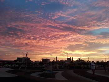 Road by buildings against sky during sunset