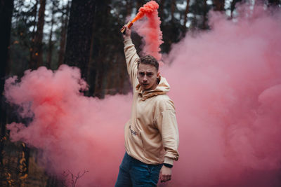 Portrait of young man holding distress flare at forest