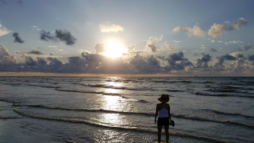 Rear view of woman standing at beach against sky during sunset