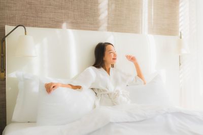 Young woman looking away while sitting on bed at home