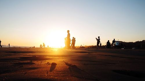 Silhouette people on beach against clear sky during sunset