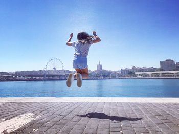 Man jumping in city against clear blue sky