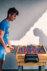 Side view of teenage boy playing foosball against wall at home