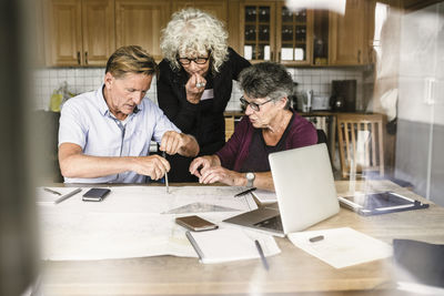 Female instructor explaining senior man and woman over laptop at table during navigation course